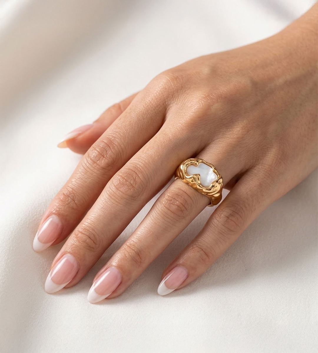 Close-up of a mother-of-pearl statement ring worn on the ring finger, showing its sculptural gold-tone frame and wide band.
