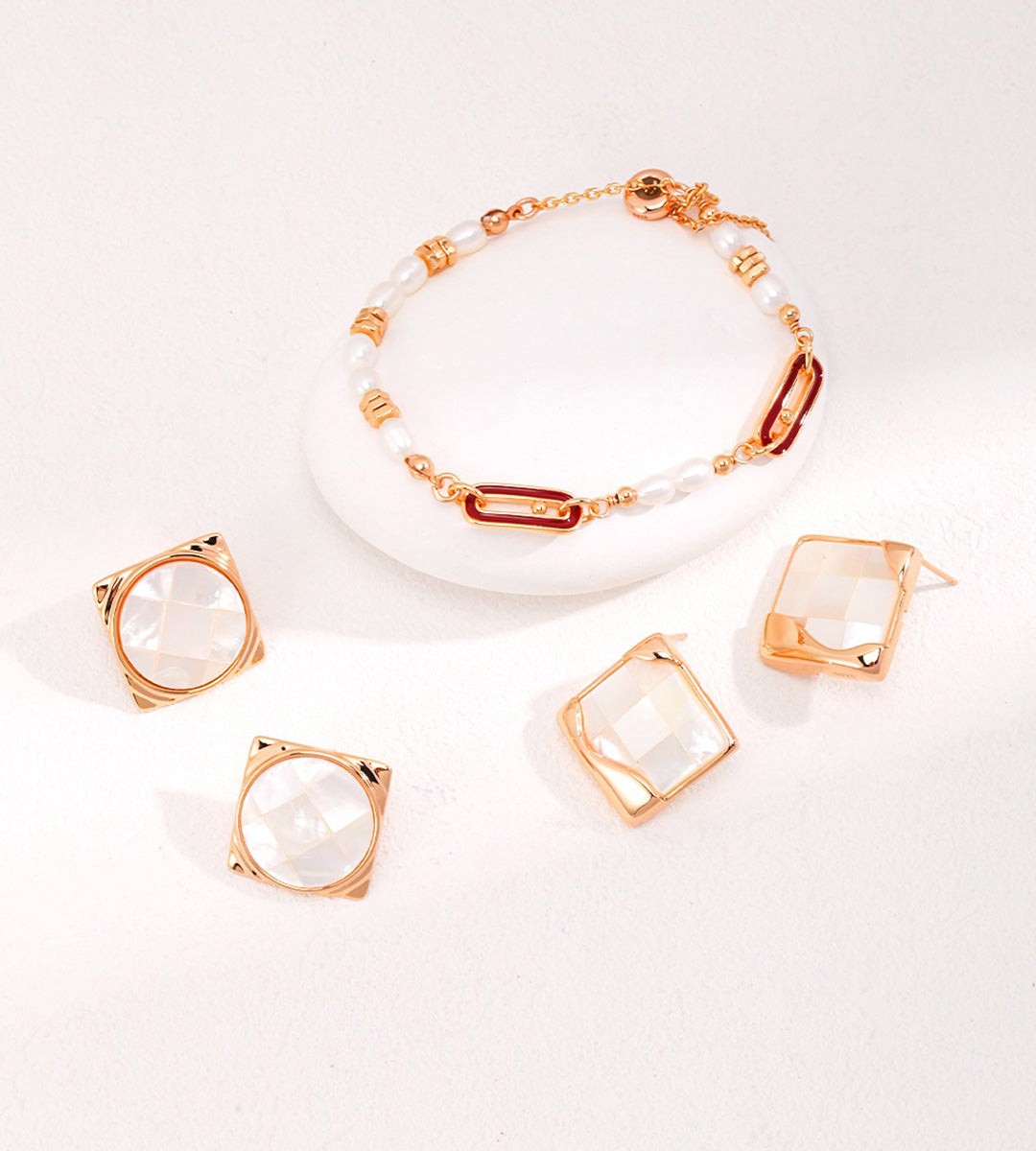 A jewelry set featuring a delicate bracelet with white beads and gold-toned links, accompanied by four matching square-cut clear mother-of-pearl stud earrings in gold settings, arranged on a white background.
