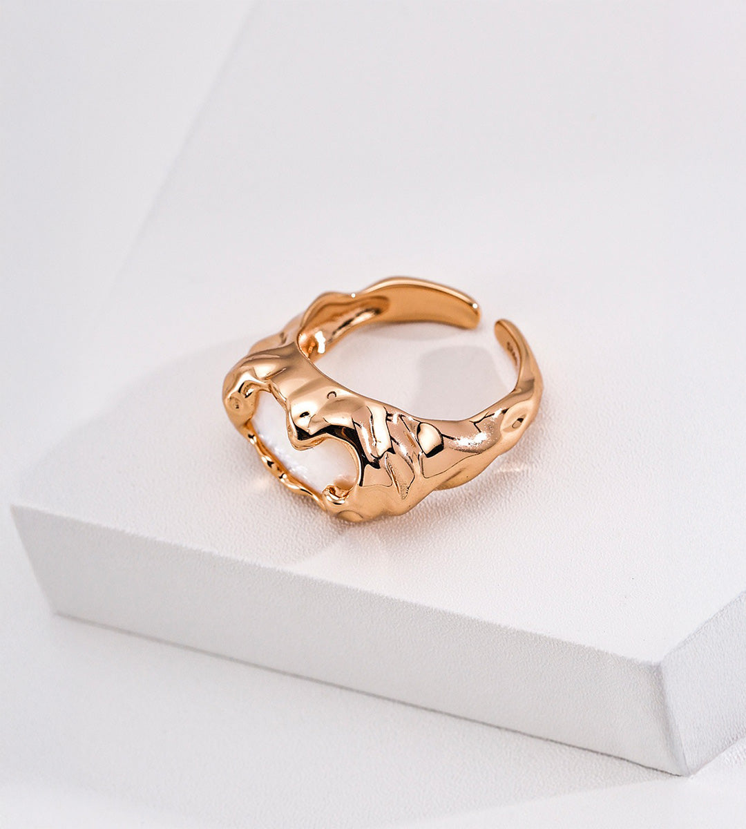 Side view of the mother-of-pearl open ring, showing flowing gold-tone contours, a wide band and adjustable gap.