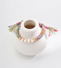 Natural pearl ethnic style adjustable braided bracelet on white ceramic display — freshwater pearls with bamboo-style 18K gold connectors, multicolour hemp cord, frayed ends, BUCKLE Collective
