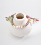 Natural pearl ethnic style adjustable braided bracelet on white ceramic display — freshwater pearls with bamboo-style 18K gold connectors, multicolour hemp cord, frayed ends, BUCKLE Collective