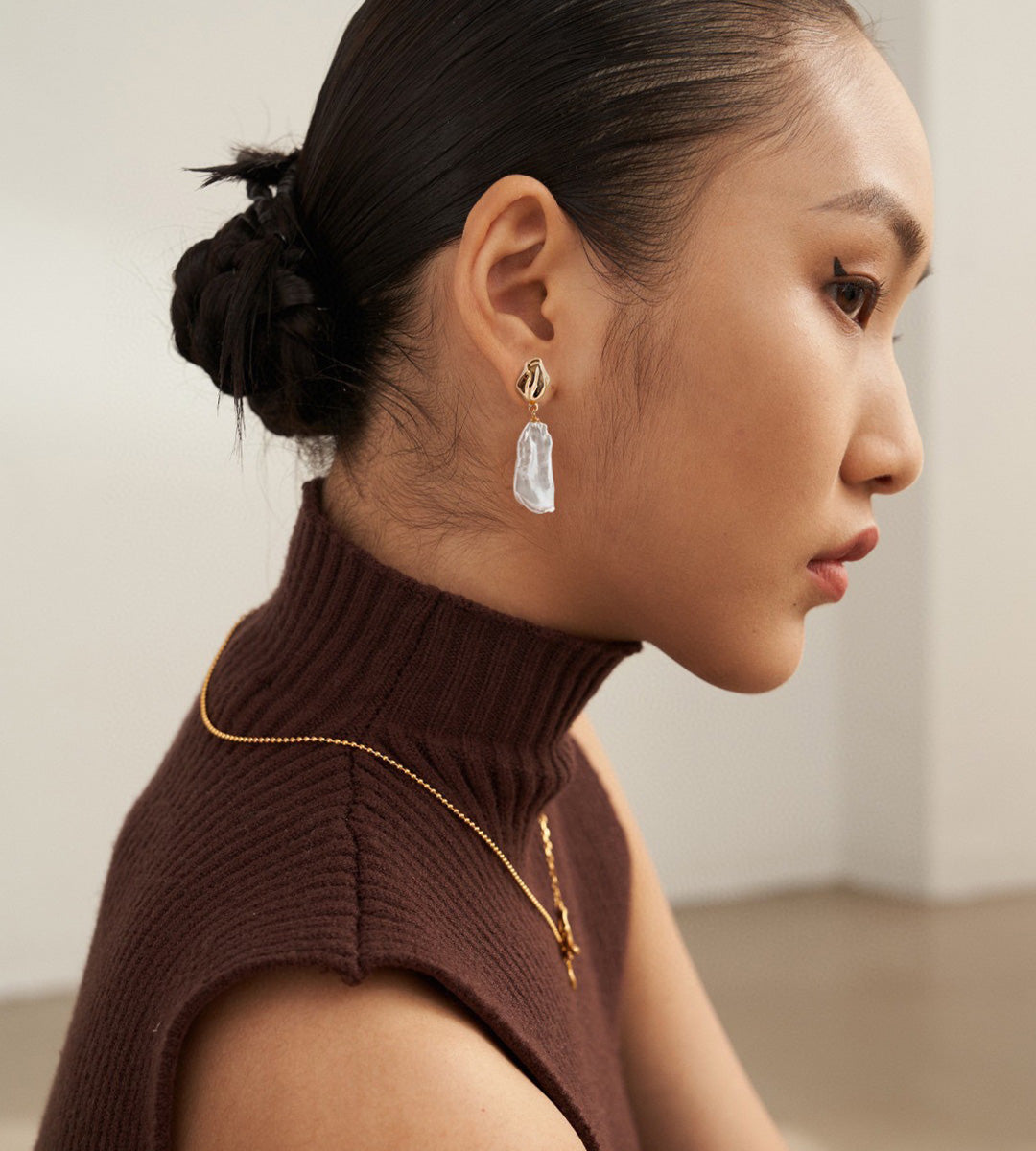 Model wearing a Vintage Gold baroque pearl drop earring with a brown high-neck knit and swept-back hair.