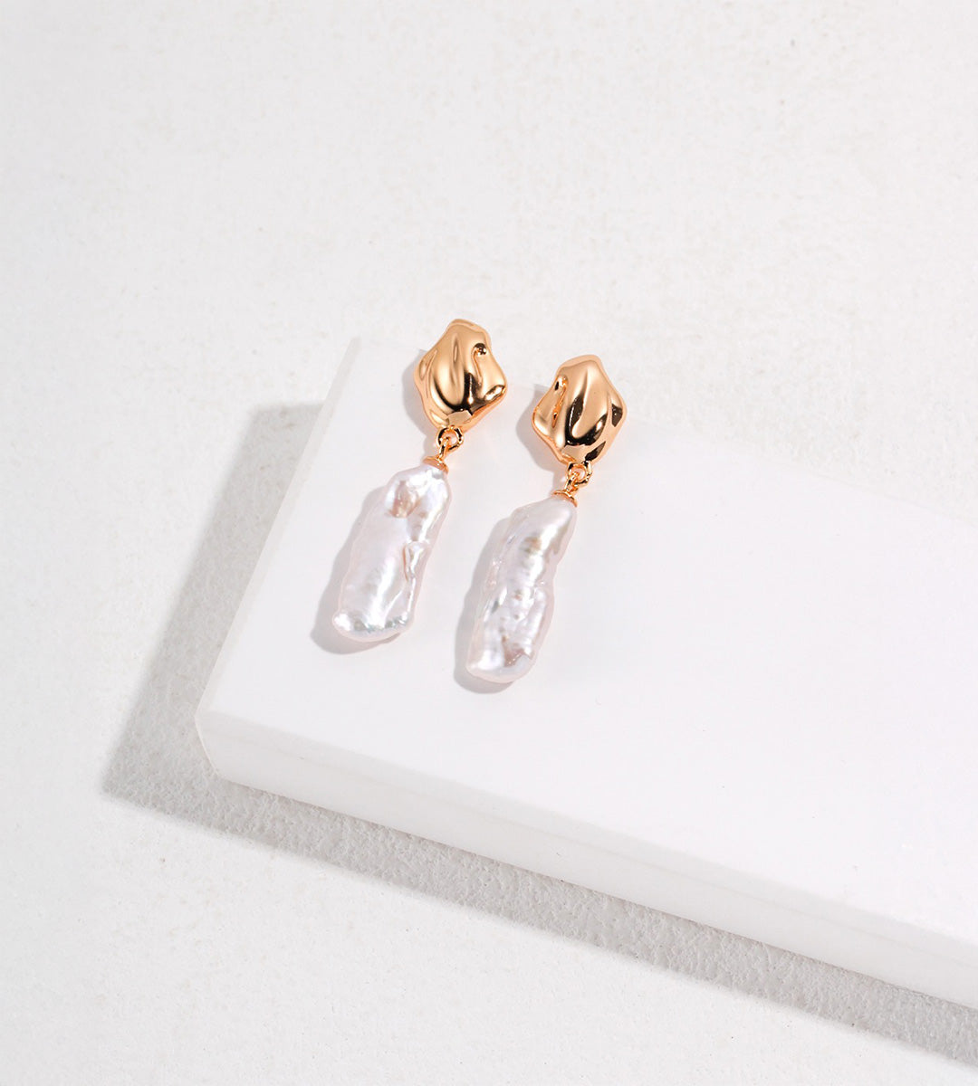 Vintage Gold baroque freshwater pearl drop earrings with sculptural tops and elongated textured pearls on a white display.