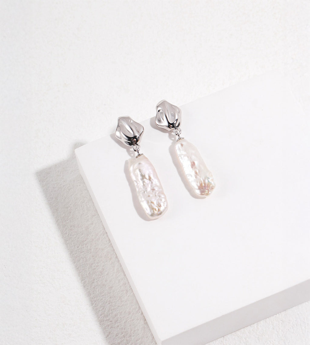 White Gold-finish S925 silver drop earrings with fluid-shaped tops and elongated, textured baroque freshwater pearls.