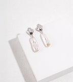White Gold-finish S925 silver drop earrings with fluid-shaped tops and elongated, textured baroque freshwater pearls.