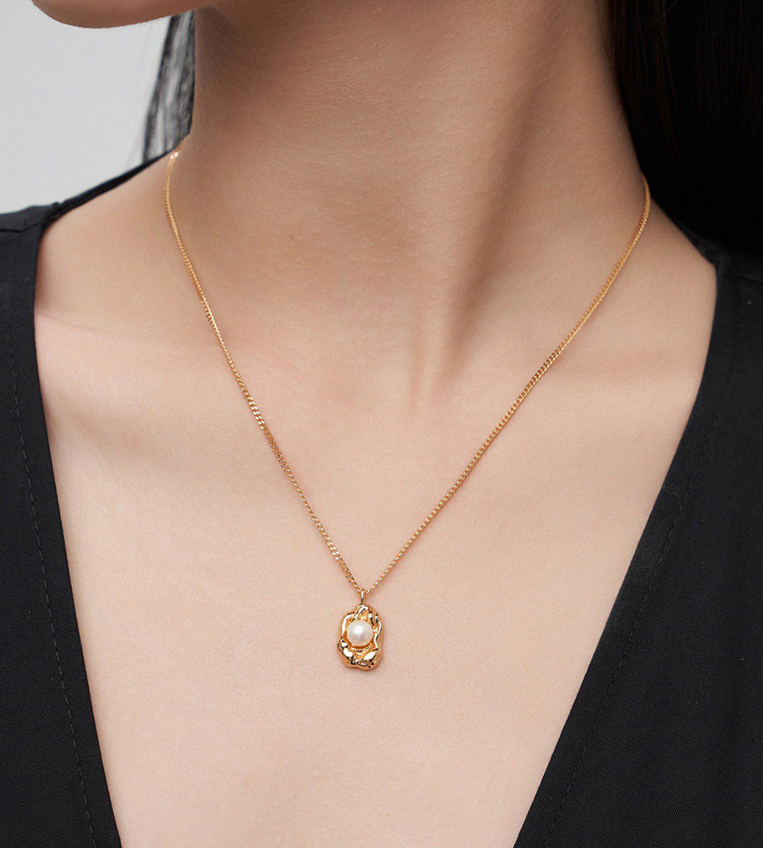 A close-up of a model's neck and chest wearing a delicate 18K gold-plated S925 silver chain necklace with an organic-shaped oval pendant featuring a white freshwater pearl in the center