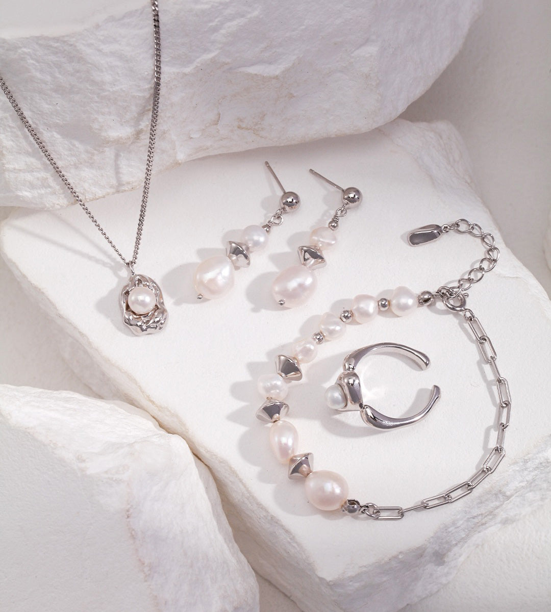 Jewelry set with freshwater pearls, including a necklace, earrings, bracelet, and ring, arranged on white textured stone blocks.