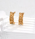 A pair of textured 18K gold-plated S925 silver hoop earrings displayed on a white ribbed surface against a light gray background.