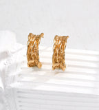 A pair of textured 18K gold-plated S925 silver hoop earrings displayed on a white ribbed surface against a light gray background.