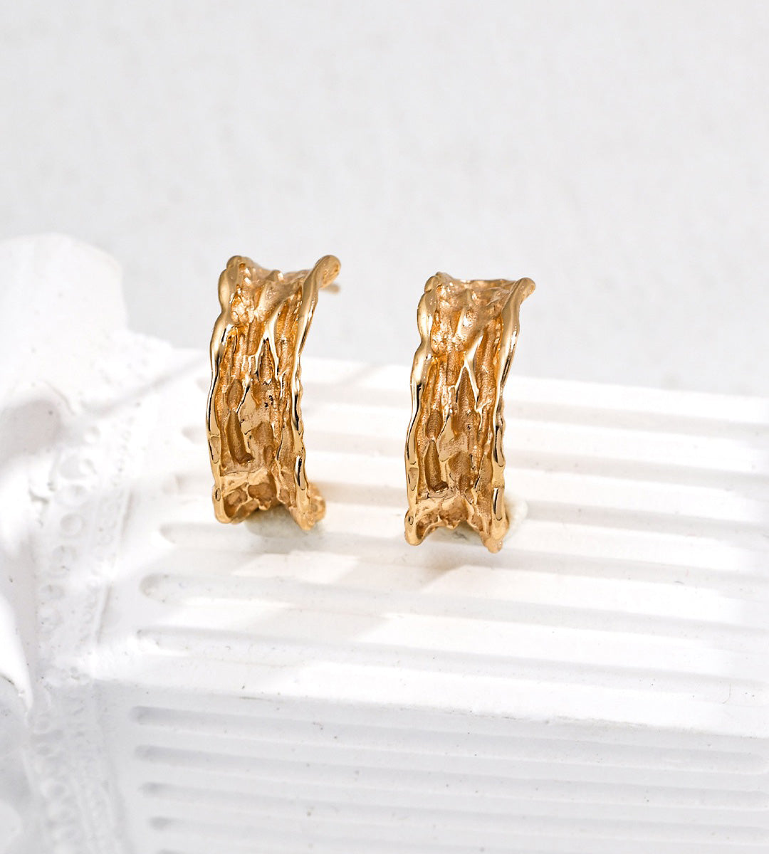 A pair of textured 18K gold-plated S925 silver hoop earrings displayed on a white ribbed surface against a light gray background.