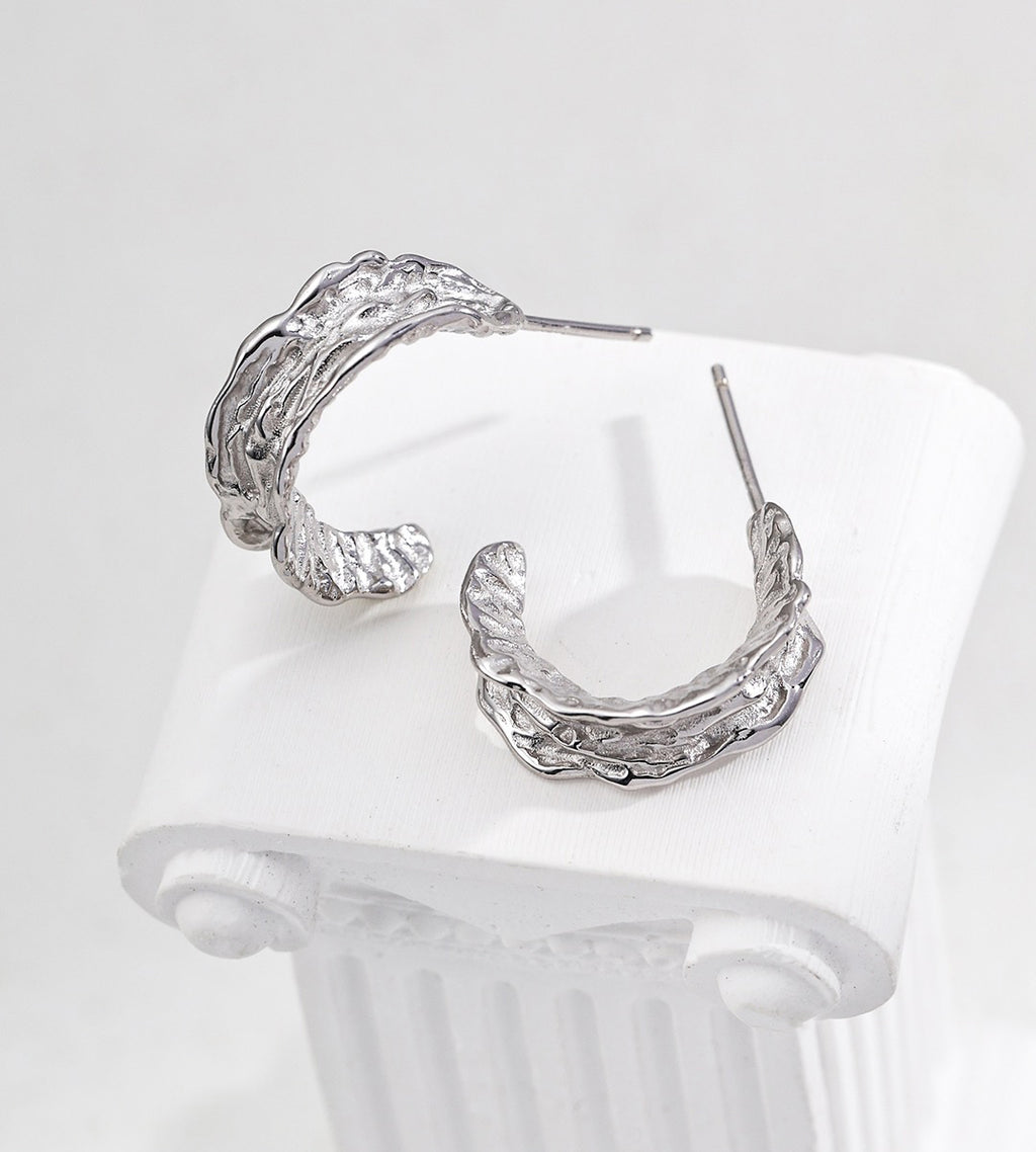 A pair of textured 18K white-gold-plated S925 silver hoop earrings displayed on a white ribbed surface against a light gray background.