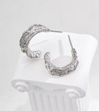 A pair of textured 18K white-gold-plated S925 silver hoop earrings displayed on a white ribbed surface against a light gray background.
