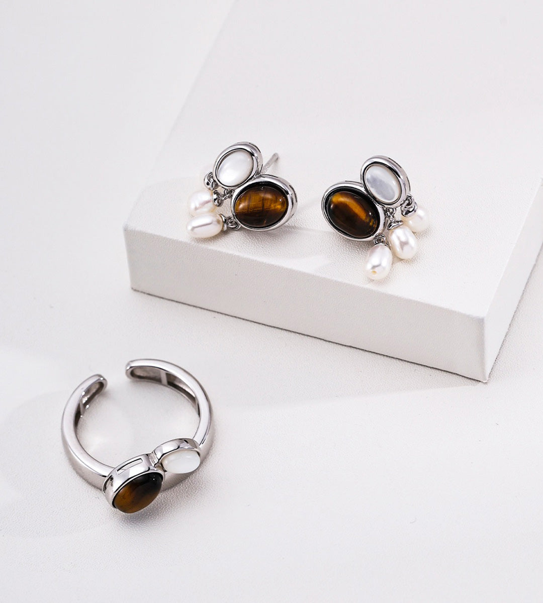 Silver-toned jewelry set featuring a pair of drop earrings with oval brown tiger's eye stones and small white pearls, alongside a matching curved hoop earring, 18K gold-plated on S925 Sterling Silver | BUCKLE Collective