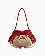 A red woven leather shoulder bag with a braided strap, paired with a beige drawstring pouch in front of it on a clean white background.