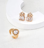 Gold-tone round cubic zirconia open ring displayed beside floral earrings with rectangular clear stones on a white sculptural stand.