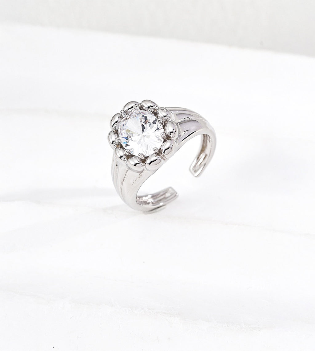 Silver-tone sculptural open ring with a round cubic zirconia centre, rounded bead surround and grooved band on a white background
