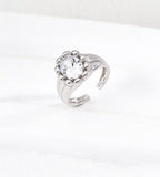 Silver-tone sculptural open ring with a round cubic zirconia centre, rounded bead surround and grooved band on a white background