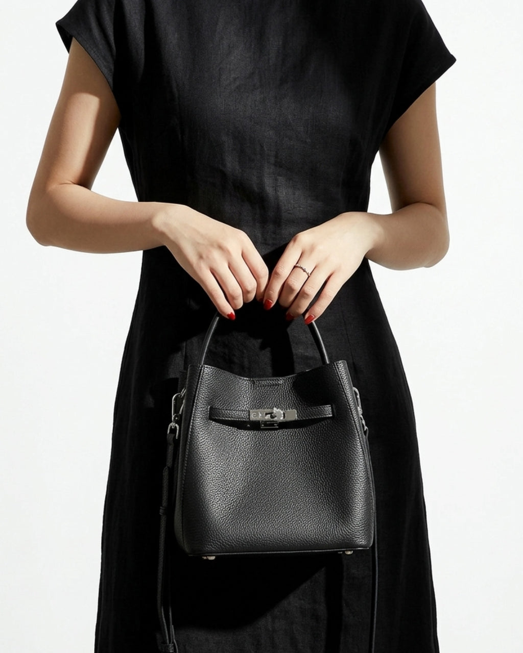 A woman in a fashion-forward black dress holds a Black Classic Genuine Leather Bucket Bag with Detachable Strap & Pouch