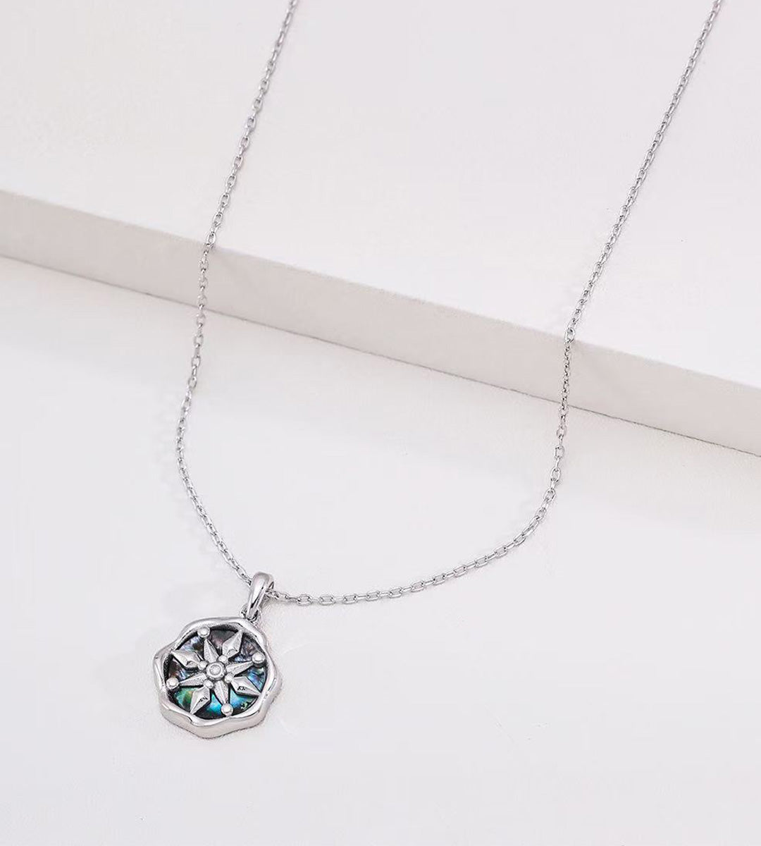 Abalone shell star compass necklace in white gold plating — eight-pointed compass motif with iridescent shell inlay, wavy octagonal border, adjustable cable chain, S925 sterling silver, BUCKLE Collective