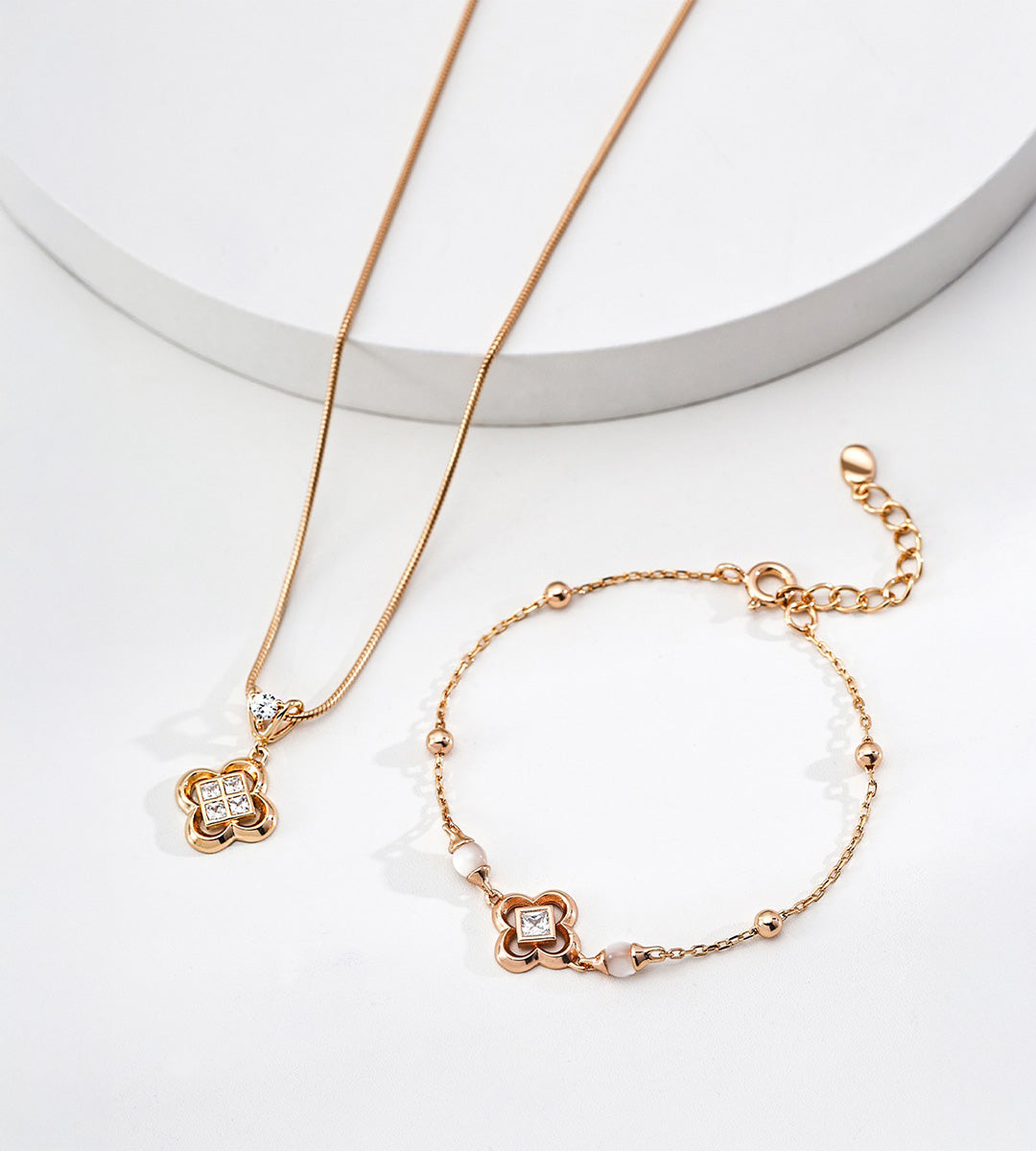 Gold-tone clover bracelet with white shell beads and square cubic zirconia, displayed beside a coordinating clover pendant necklace.