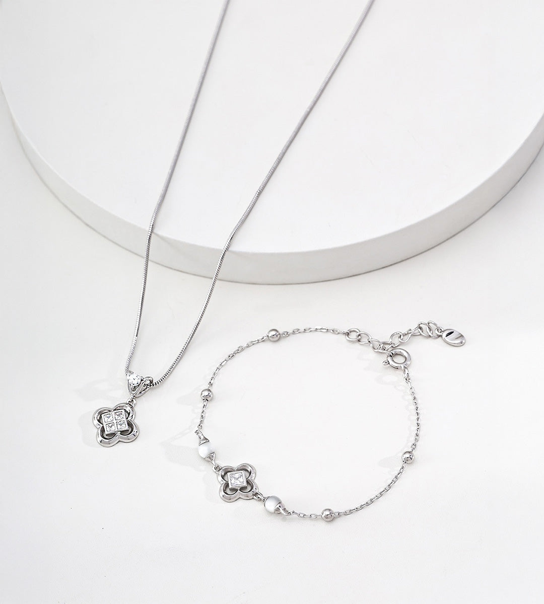 Silver-tone clover bracelet with white shell beads and square cubic zirconia, displayed beside a coordinating clover pendant necklace