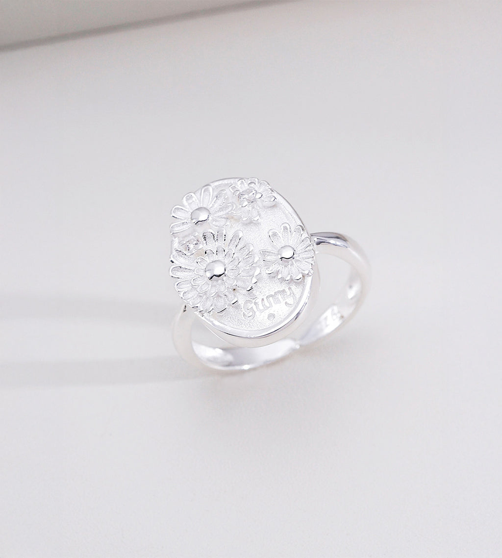 Sunny Daisy embossed open ring in natural silver tone — 3D raised daisy floral oval signet plaque with engraved "sunny" lettering, adjustable open band, 18K plated S925 sterling silver, BUCKLE Collective
