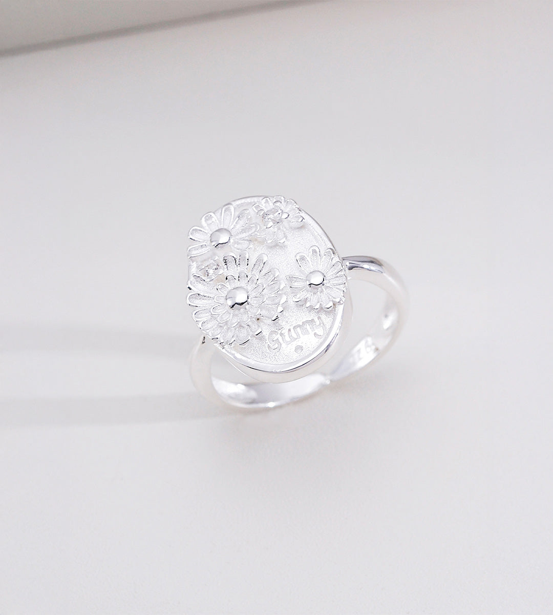 Sunny Daisy embossed open ring in natural silver tone — 3D raised daisy floral oval signet plaque with engraved "sunny" lettering, adjustable open band, 18K plated S925 sterling silver, BUCKLE Collective