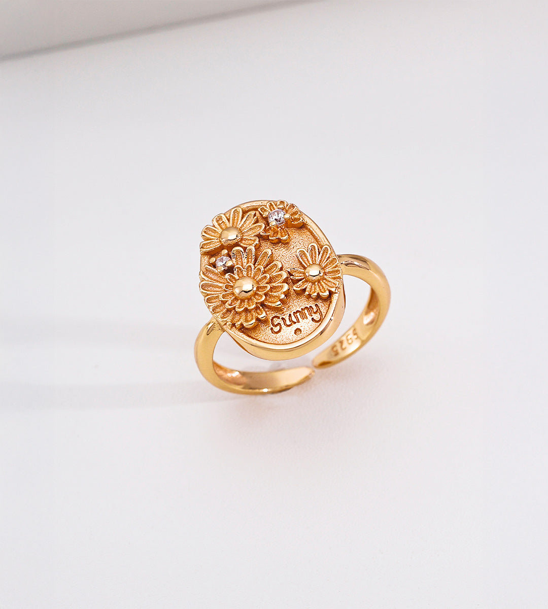 Sunny Daisy embossed open ring in vintage gold — 3D raised daisy blooms with engraved "sunny" lettering and pavé cubic zirconia accents on oval signet plaque, 18K gold plated S925 sterling silver, BUCKLE Collective