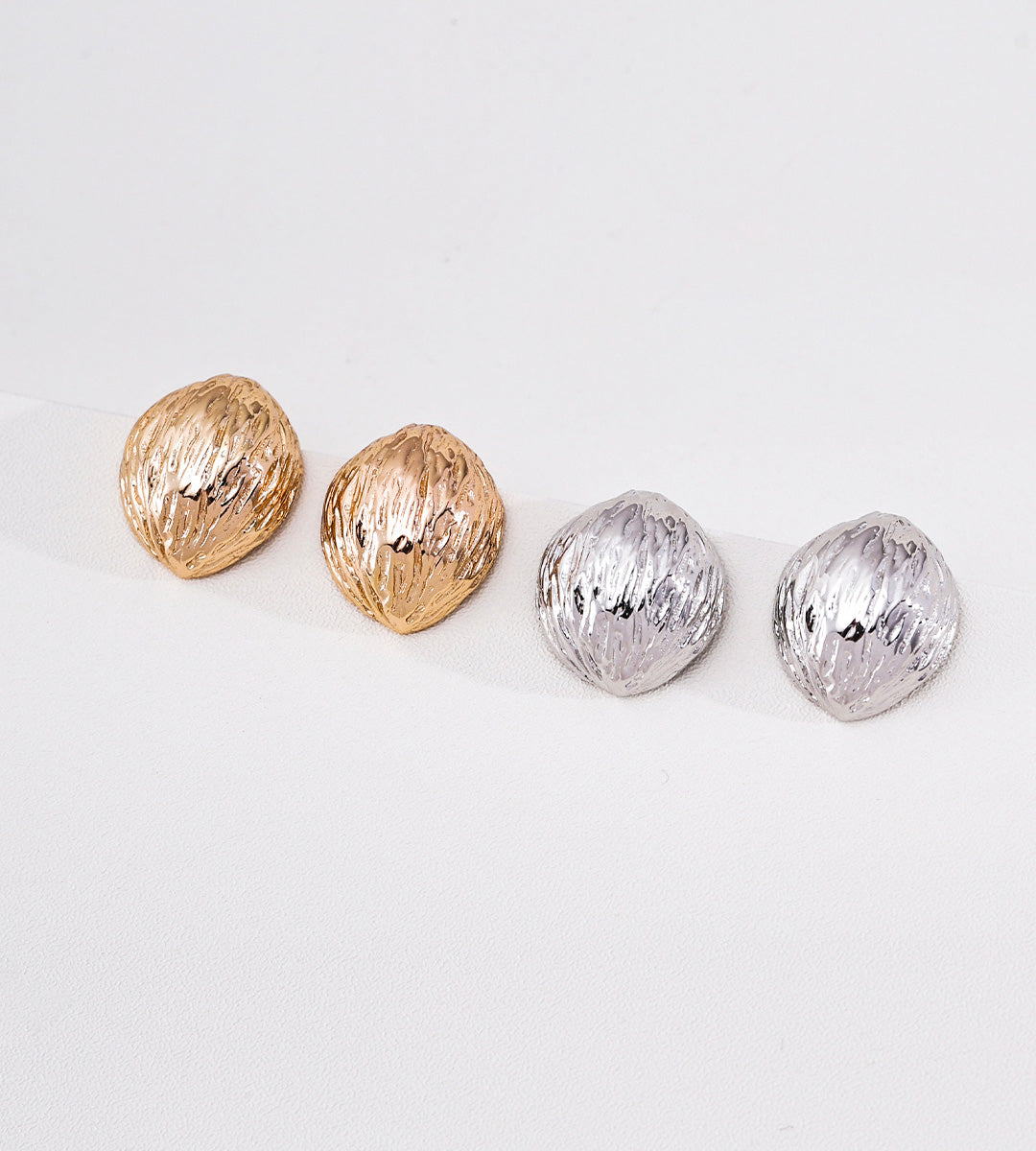 Four textured, rounded nut-shaped stud earrings arranged in a row on a plain white background, including two gold-toned and two silver-toned pairs.