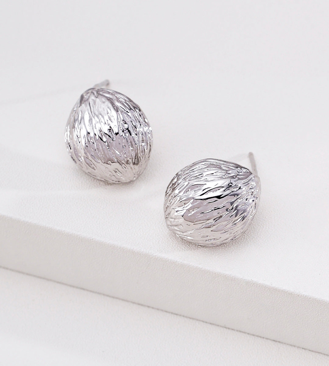 A pair of textured 18K white-gold-plated S925 silver dome stud earrings with a hammered, organic surface finish, displayed on a clean white surface.