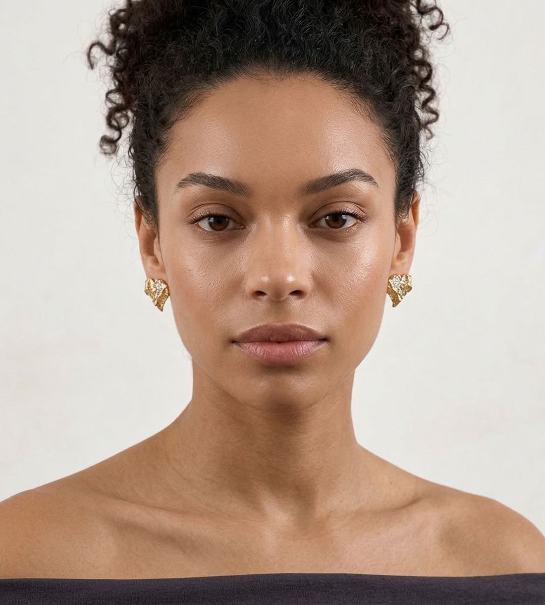 Front view of a model wearing Vintage Gold textured heart stud earrings with cubic zirconia accents and a black off-shoulder top.