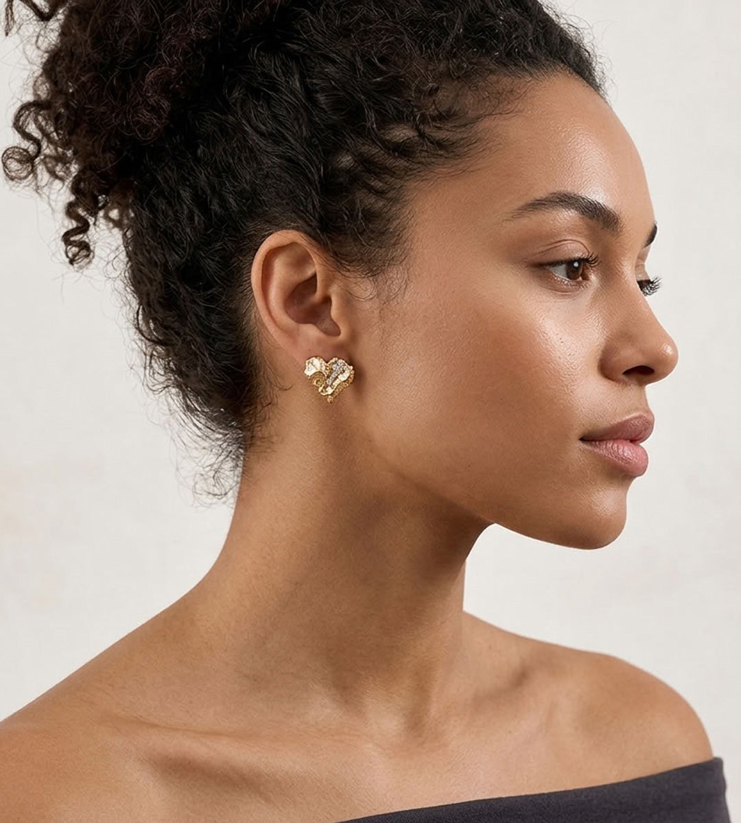 Side view of a model wearing a Vintage Gold heart stud earring, showing its sculptural rock texture and cubic zirconia detail.