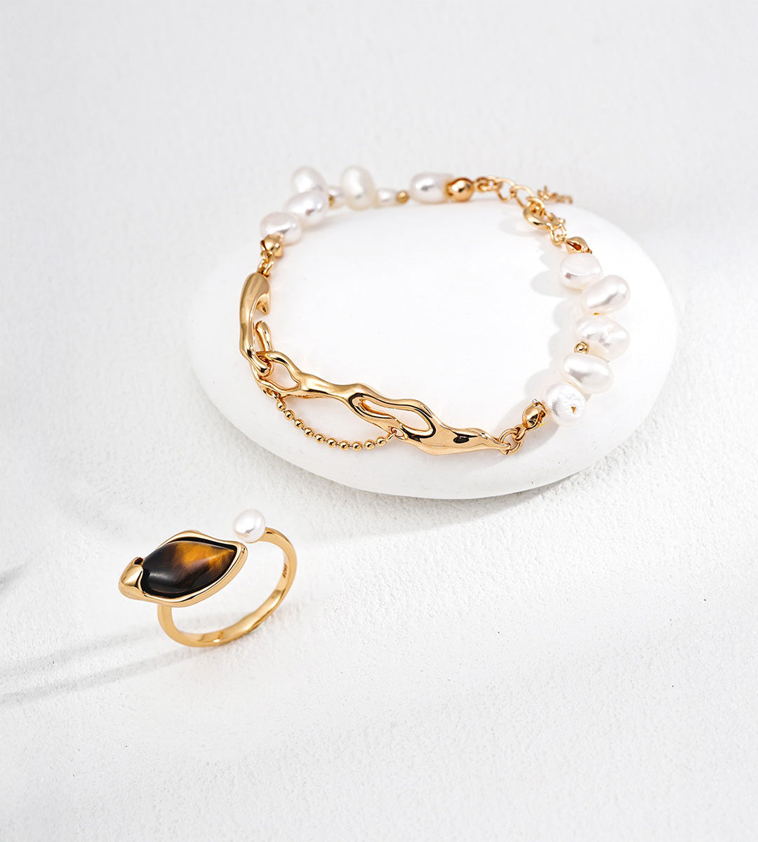 Tiger’s eye and freshwater pearl open ring in Vintage Gold beside a pearl bracelet with sculptural gold-tone links.