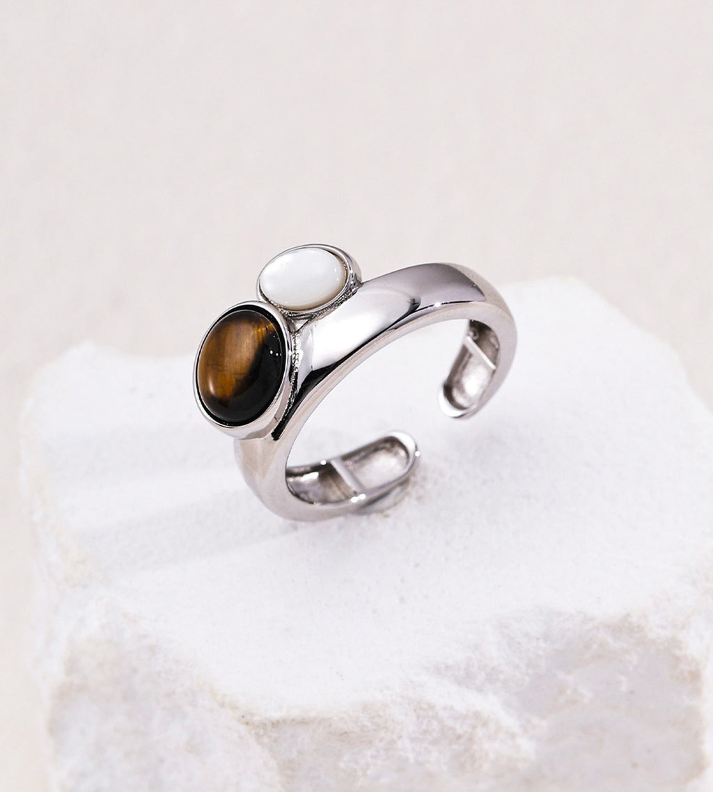 An 18K White-Gold-Plated open cuff ring featuring two oval inlays: a prominent brown tiger's eye stone and a smaller mother-of-pearl | BUCKLE Collective