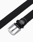 A close-up of a black braided woven belt with a silver metal buckle and a black leather keeper loop by BUCKLE Collective