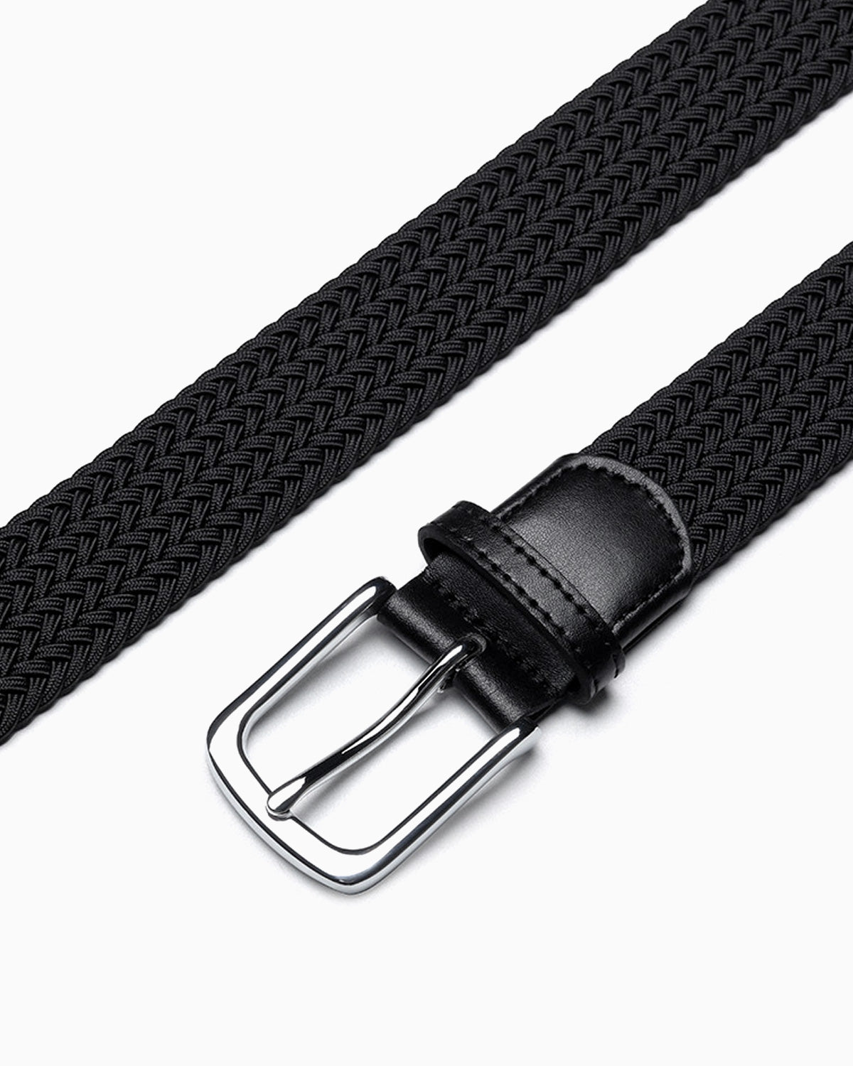 A close-up of a black braided woven belt with a silver metal buckle and a black leather keeper loop by BUCKLE Collective