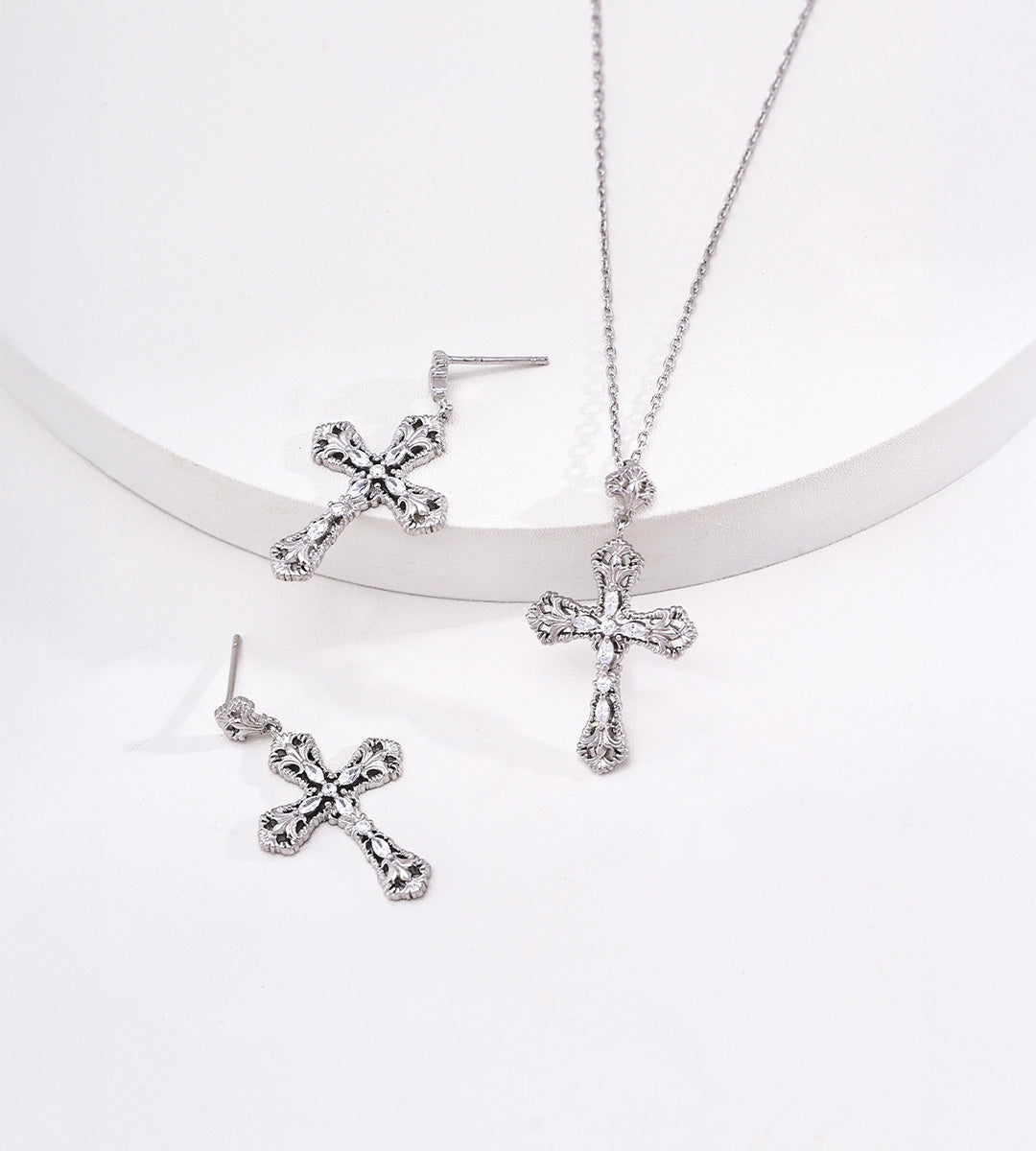 White Gold-finish engraved cross necklace displayed beside matching silver-tone cross drop earrings.