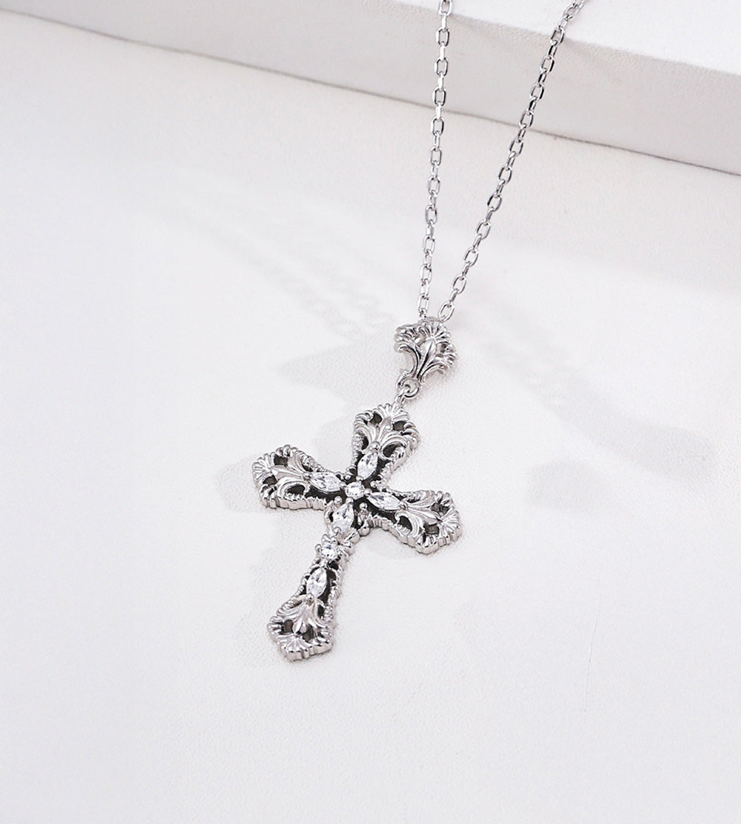 White Gold-plated S925 silver cross necklace with ornate scrollwork and cubic zirconia accents on a white display.