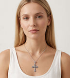 A woman with blonde hair wearing a silver cross pendant necklace and a white tank top, shown from the chest up against a light gray background.