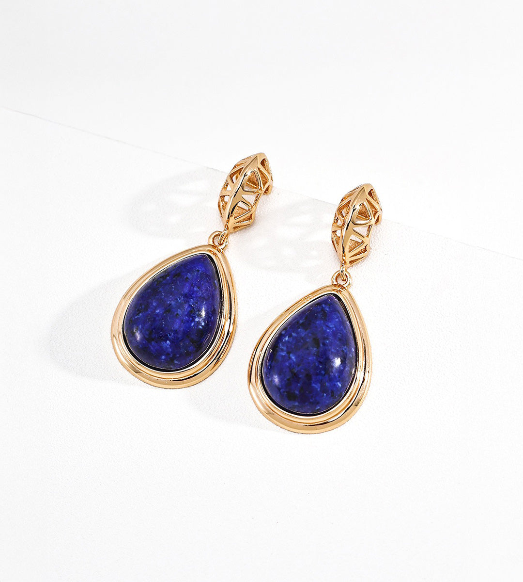 A pair of 18K gold-plated teardrop dangle earrings with deep blue lapis lazuli stones, displayed on a clean white background.