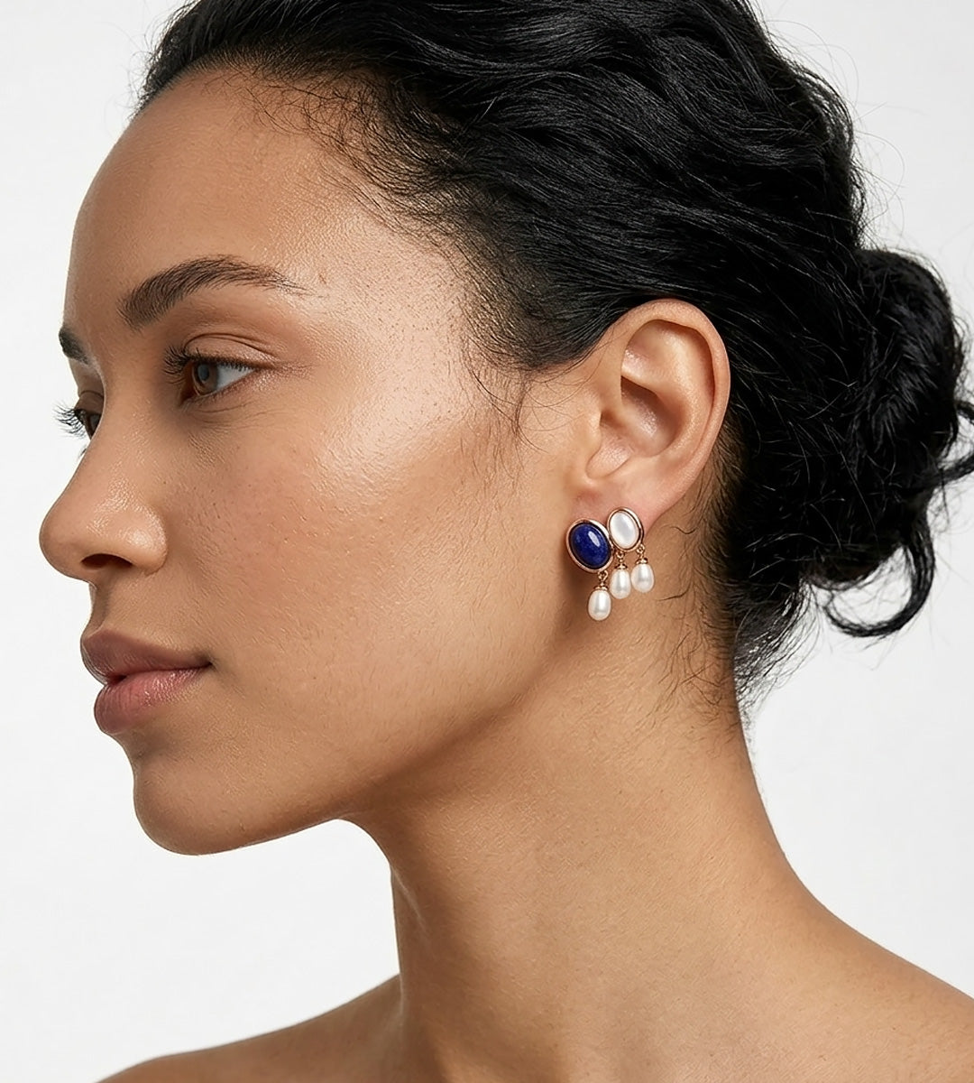A close-up side profile of a woman wearing a pair of 18K gold-plated S925 Silver drop earrings with a lapis lazuli oval stone, mother-of-pearl, and three small natural freshwater AAAA-grade pearls. BUCKLE Collective