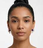 A close-up portrait of a woman with her hair in a bun, wearing a pair of 18K gold-plated S925 Silver drop earrings with a lapis lazuli oval stone, mother-of-pearl, and three small natural freshwater AAAA-grade pearls. BUCKLE Collective