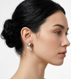 A close-up side profile of a woman with dark hair in a bun, wearing a unique drop earring featuring a round tiger's eye gemstone, mother-of-pearl, and three small natural freshwater white pearls. BUCKLE Collective