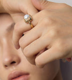 Close-up of a model wearing a gold-tone square pearl ring, showing the raised pearl and hammered-texture frame.