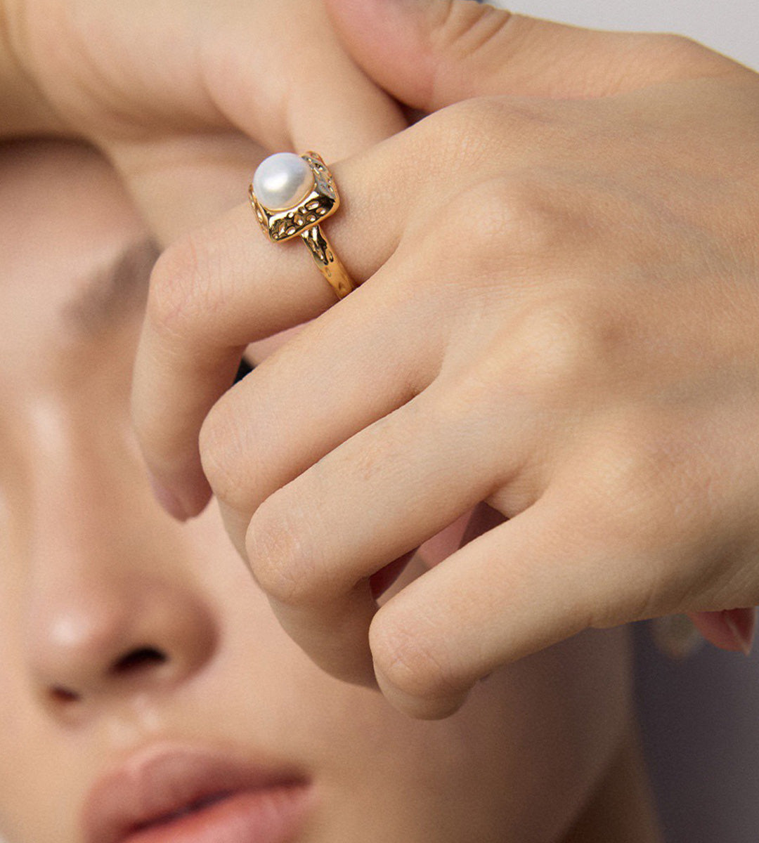 Close-up of a model wearing a gold-tone square pearl ring, showing the raised pearl and hammered-texture frame.