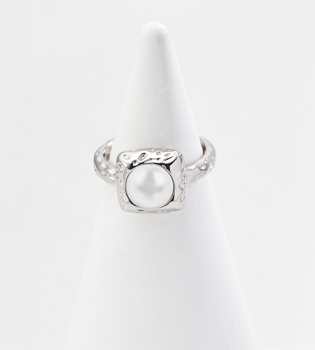 Silver-tone pearl ring with a square hammered-texture frame and matching textured band on a white cone display.