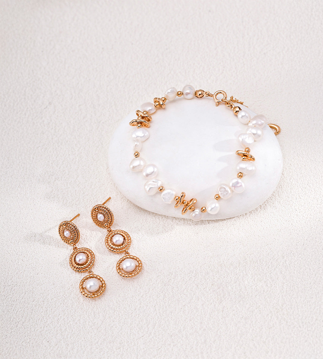 Vintage Gold three-tier pearl drop earrings displayed beside a pearl bracelet with gold-tone accents on a white background.