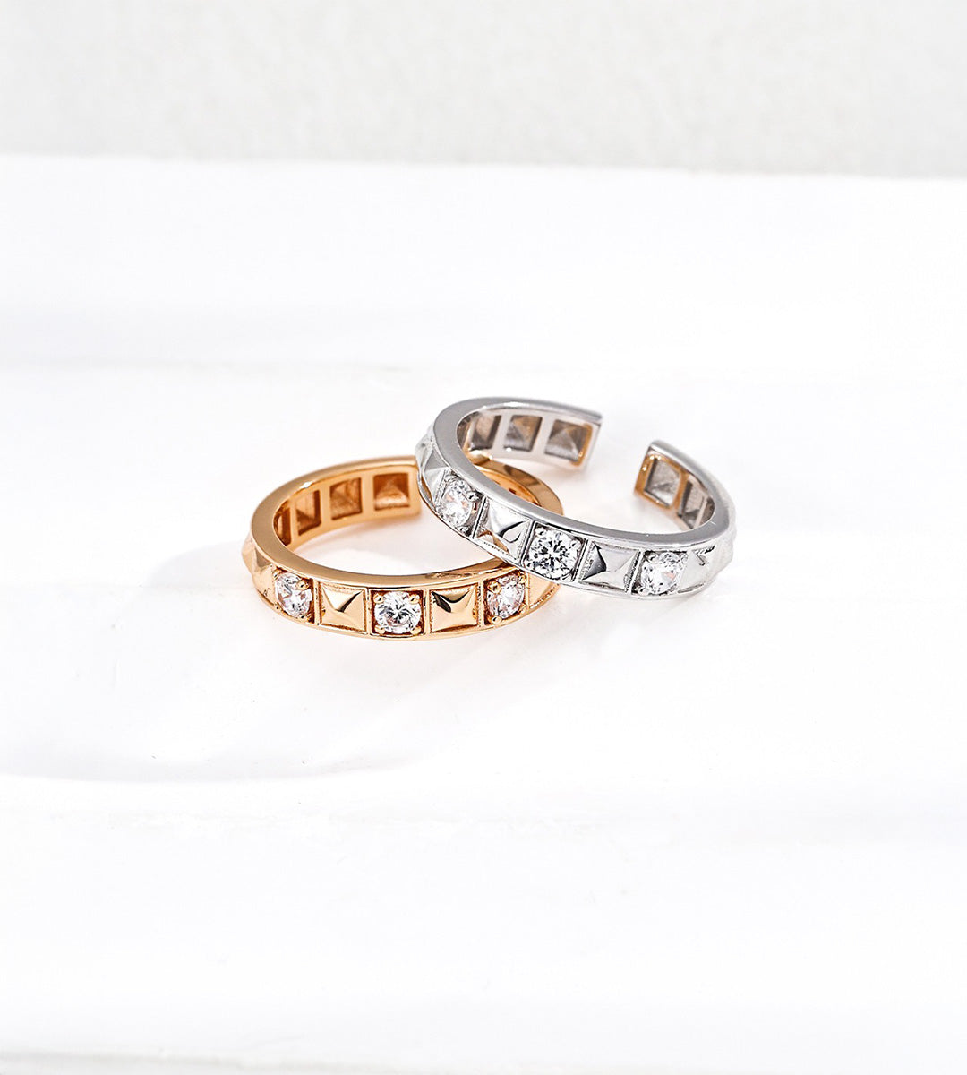 Gold-tone and silver-tone rivet rings overlapping, showing alternating pyramid details, cubic zirconia stones and open adjustable bands.