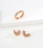 Gold-tone rivet and cubic zirconia open ring displayed above fan-shaped pearl and clear-stone earrings on white blocks.