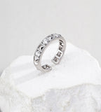 Silver-tone open ring with alternating pyramid-shaped rivets and round cubic zirconia, standing on a white stone block.